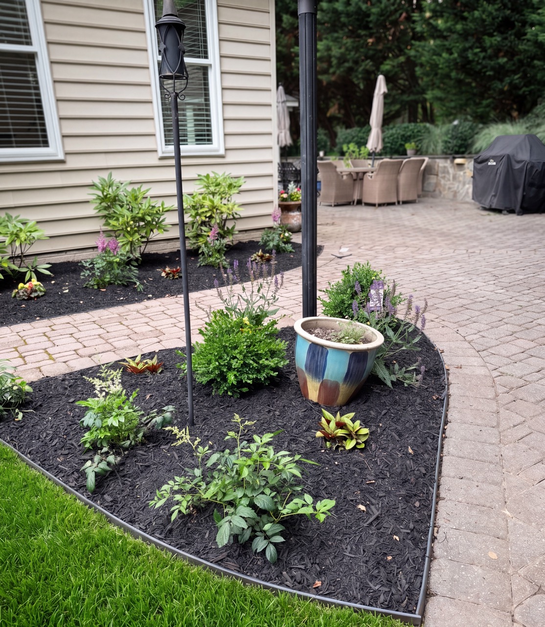 Curved patio-side landscape bed with shrubs and container planter by Green Life Landscaping